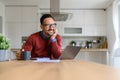 Thoughtful smiling businessman with hand on chin looking away while sitting at desk in home office Royalty Free Stock Photo