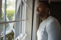 Thoughtful smiling man looking out through window at home