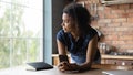 Thoughtful smiling millennial Afro American girl holding mobile phone Royalty Free Stock Photo