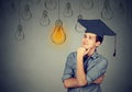 Thoughtful student in cap gown looking up at light bulb