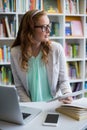 Thoughtful teacher using digital tablet with laptop and phone on table in library Royalty Free Stock Photo