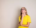 Thoughtful teen girl in eyeglasses looking up. Pretty casual thinking teenager in glasses and yellow t-shirt looking up with Royalty Free Stock Photo