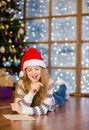 Thoughtful teen girl in red christmas hat writes letter to Santa Claus Royalty Free Stock Photo