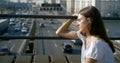 Thoughtful teenage girl is watching moving cars over road sitting on bridge in city in summer Royalty Free Stock Photo
