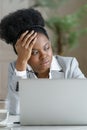 Thoughtful tired Afro businesswoman wear headphones looking at window, working at laptop, close up. Royalty Free Stock Photo