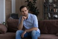 Thoughtful upset man looking in distance, sitting on couch alone