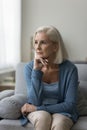 Thoughtful upset middle-aged woman sit on sofa at home