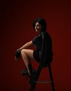 Thoughtful woman in black tight dress, leather jacket and big brutal boots sitting on a stepladder and looks down on red Royalty Free Stock Photo