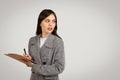 Thoughtful woman with clipboard on grey background, free space Royalty Free Stock Photo