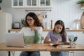 Focused woman freelancer with laptop sitting at kitchen table with daughter doing school assignments Royalty Free Stock Photo