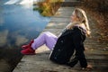 Thoughtful woman sitting on the edge of wooden jetty by the lake with autumn reflections