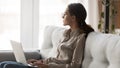 Thoughtful woman sitting on sofa with laptop thinking of inspiration