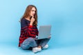 Woman sitting with crossed legs, holding laptop on knees, working online, having pensive expression. Royalty Free Stock Photo