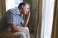 Thoughtful worried senior caucasian man sitting on sofa and looking through window Royalty Free Stock Photo
