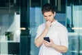 Thoughtful and worried young man, businessman, freelancer looks at the phone, received bad news Royalty Free Stock Photo