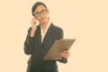 Thoughtful young Asian businesswoman holding clipboard while talking on mobile phone Royalty Free Stock Photo