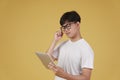 Thoughtful young asian man dressed casually thinking using digital tablet isolated on yellow background