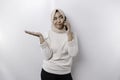 A thoughtful young Asian Muslim woman wearing a hijab and pointing copy space beside her while talking on the phone isolated by a Royalty Free Stock Photo