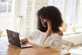 Thoughtful young black businesswoman brunette typing on laptop and answering mobile call. Royalty Free Stock Photo