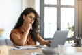 Thoughtful young brunette woman looking at laptop screen, working online at desk in home office, free space Royalty Free Stock Photo