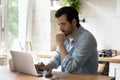 Thoughtful young businessman working remotely on computer in kitchen. Royalty Free Stock Photo