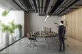 Thoughtful young businessman standing in modern coworking office interior with equipment, furniture, decorative plants and matte