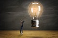 Thoughtful businesswoman with glowing light bulb in modern room with wooden flooring. Success, idea and innovation concept Royalty Free Stock Photo