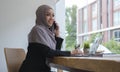 Thoughtful young businesswoman in hijab having conversation on mobile phone while sitting in bright modern office Royalty Free Stock Photo