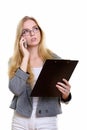 Thoughtful young businesswoman holding clipboard and talking on Royalty Free Stock Photo