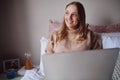 Thoughtful young businesswoman working on laptop from home in her bedroom - student learning new things online