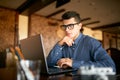 Thoughtful young caucasian businessman in glasses working on laptop computer. Pensive attractive hipster freelancer Royalty Free Stock Photo