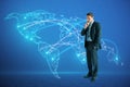 Thoughtful young european businessman with abstract glowing map hologram on blue background. Digital world, network and technology Royalty Free Stock Photo