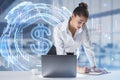 Thoughtful young european businesswoman leaning and writing on desktop with laptop and glowing dollar hologram on bright blurry