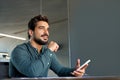 Thoughtful young Latin business man using mobile phone at work in office. Royalty Free Stock Photo