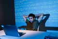 Thoughtful young male developer focused on laptop, debugging code late at night as blue light and projected code lines Royalty Free Stock Photo