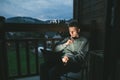 Thoughtful young man sits in the evening on a chair on a balcony in a country apartment and uses a laptop, looking at a screen Royalty Free Stock Photo