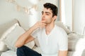 Thoughtful young man sitting on the bed in the bedroom, touching his chin and thinking. Thoughtful mature man resting on Royalty Free Stock Photo