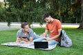 Thoughtful young man is sitting with a laptop on grass on a college campus and taking notes in notebook. Man explaining something Royalty Free Stock Photo