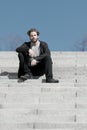 Thoughtful young man sitting on steps against blue sky background Royalty Free Stock Photo