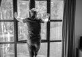 Thoughtful young man standing near the whole-wall window and looking out the street and thinking about something. Self-isolation, Royalty Free Stock Photo