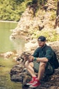 Single male hiker using tablet on nature while sitting on rocky river shore