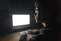Thoughtful young man using blank screen computer in dark room Royalty Free Stock Photo