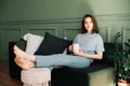 A thoughtful young middle-aged woman enjoying a rest and a cup of tea on the couch, pondering, looking at the open space Royalty Free Stock Photo