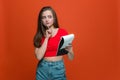 Thoughtful young modern girl with notebook create ideas, planning goals, aims, invent decision on orange background