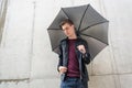 Thoughtful young teen man standing in rain in city with umbrella