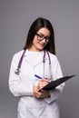 Thoughtful young woman doctor thinking and writing on clipboard over greybackground Royalty Free Stock Photo