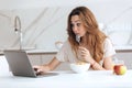 Thoughtful young woman eating and using laptop Royalty Free Stock Photo