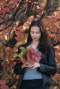 Thoughtful young woman in forest. Portrait of brunette girl with autumn leaves in her hands. Vertical frame Royalty Free Stock Photo