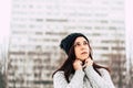 Thoughtful young woman in gray knitted sweater and hat standing on street in winter season. Pretty brunette looking away Royalty Free Stock Photo