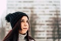 Thoughtful young woman in gray knitted sweater and hat standing on street in winter season. Pretty brunette looking away Royalty Free Stock Photo